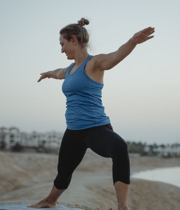 A person in a fluid warrior yoga pose on a beach, radiating strength against a sunset.